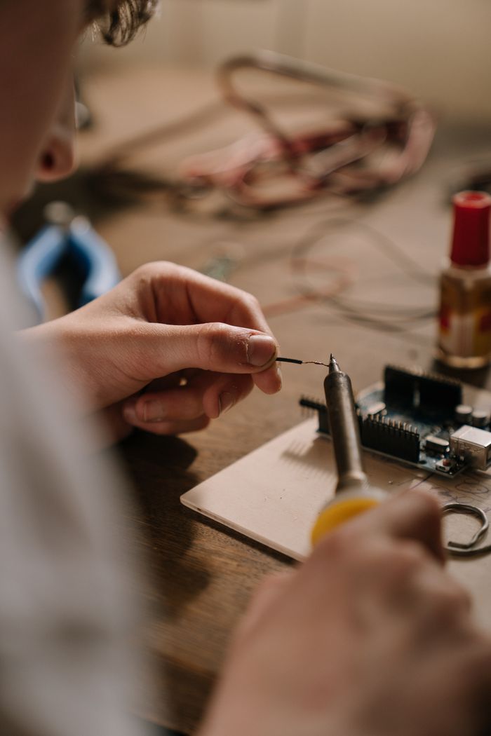 Home A person using a soldering iron to work on a circuit board, focused on precise electronic repair.